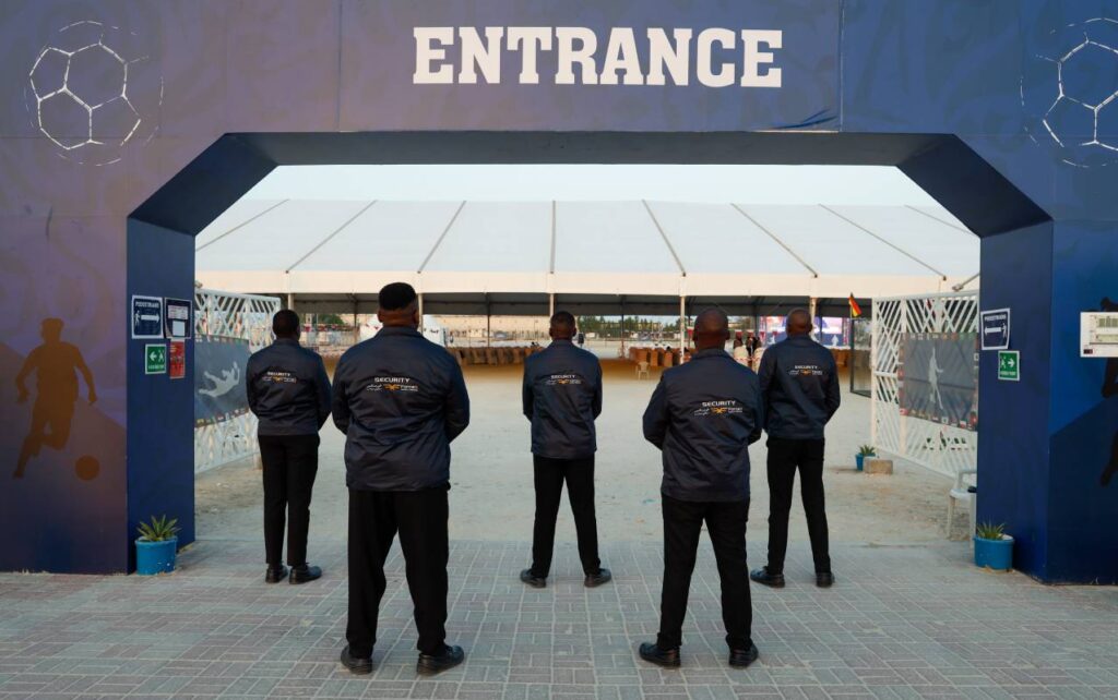A group of five Event Security in Qatar personnel from the company ForceX Security Services stand with their backs to the camera, guarding a large entrance archway labeled "ENTRANCE.